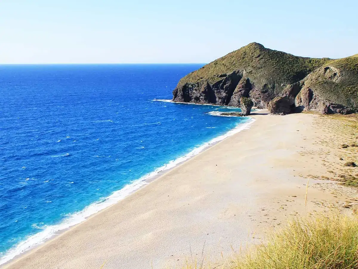 Playa de los Muertos en Cabo de Gata-Níjar, con arena dorada, mar azul intenso y acantilados verdes.