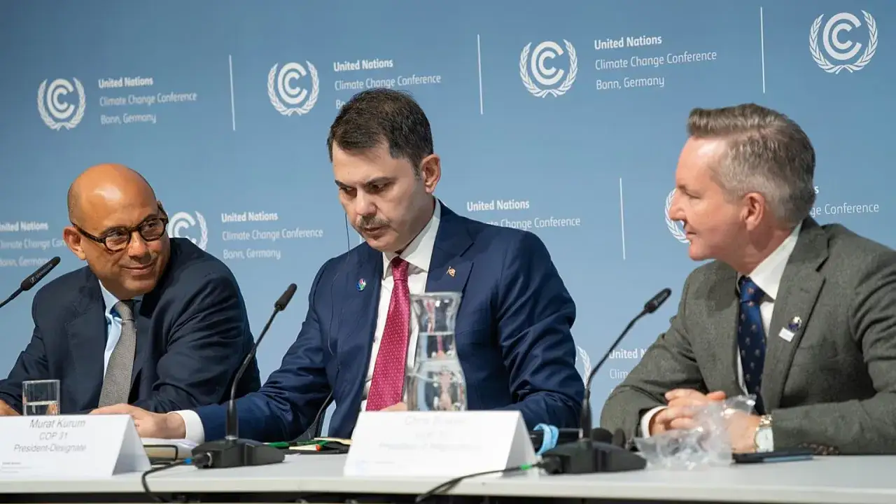 Drei Teilnehmer der Klimakonferenz in Bonn diskutieren. Ein Mann mit Brille l&auml;chelt, w&auml;hrend ein anderer nachdenklich blickt.