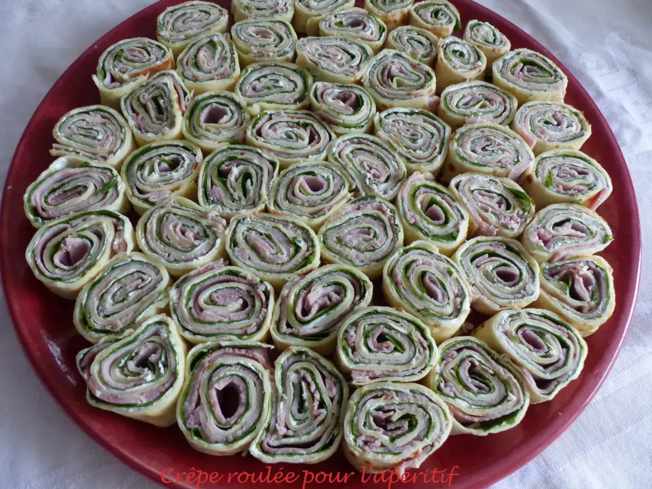 Assiette de cr&ecirc;pes roul&eacute;es garnies de jambon, fromage frais et herbes, parfaites pour un ap&eacute;ritif convivial.