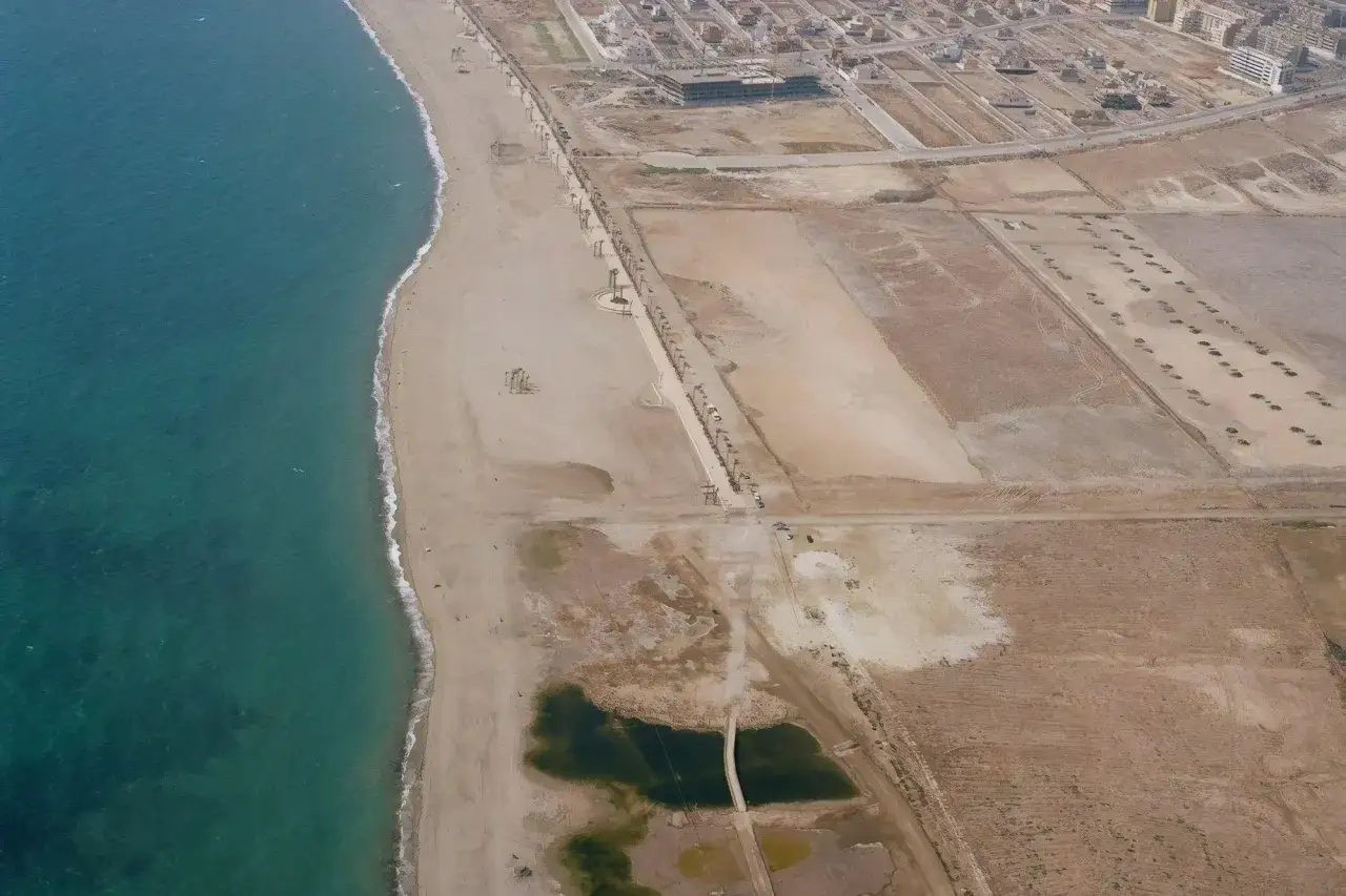Vista aérea de la playa de las salinas, con el mar turquesa a la izquierda y la arena dorada extendiéndose hacia la urbanización.