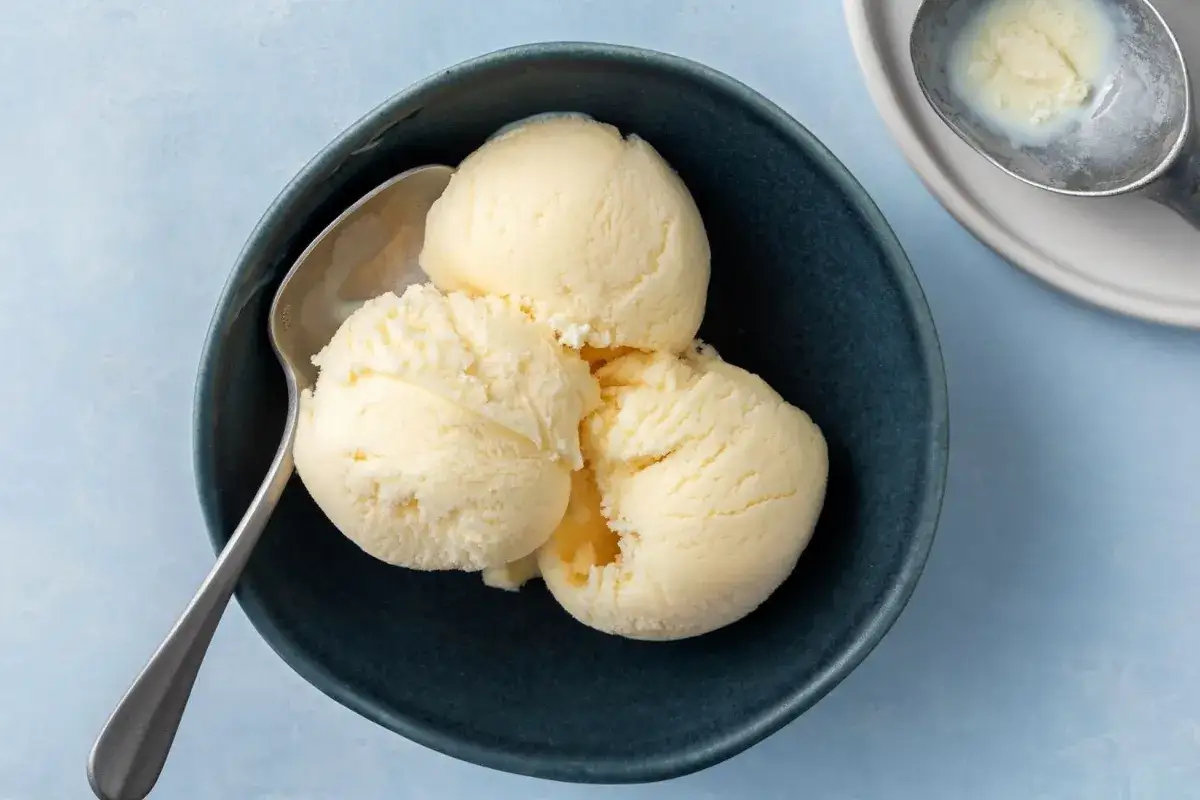 Tre skopor kr&auml;mig vaniljglass i en m&ouml;rkbl&aring; sk&aring;l, redo att avnjutas. Perfekt f&ouml;r ett enkelt gelato recept.