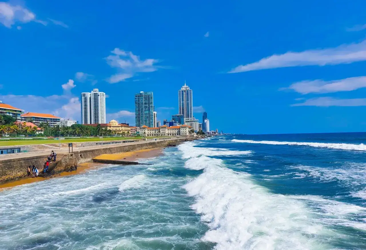 Letnie fale rozbijają się o brzeg w Kolombo. W oddali widać nowoczesne wieżowce, a na plaży kilka osób cieszy się słońcem. Sri Lanka w lipcu zachwyca!