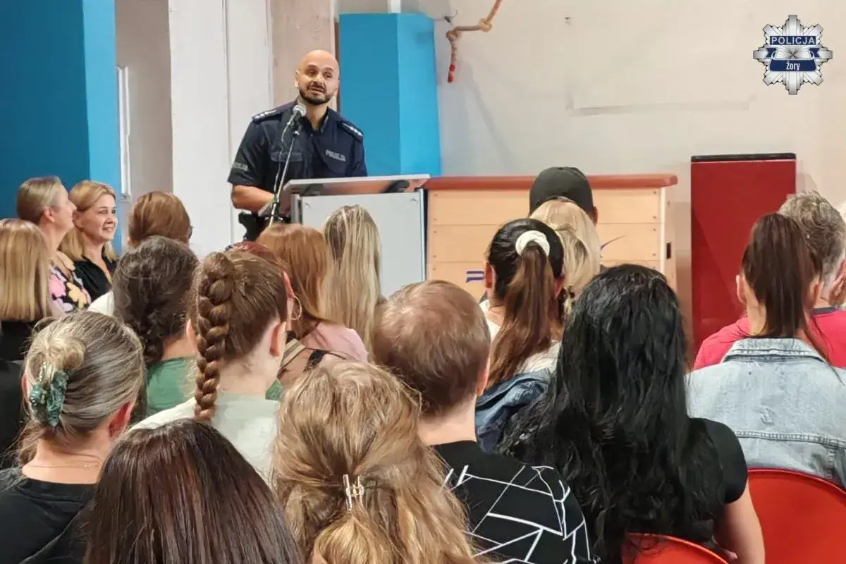 Policjant przemawia do grupy osób, wśród których są dzieci. Temat: przesłuchanie dziecka w szkole bez zgody rodziców.