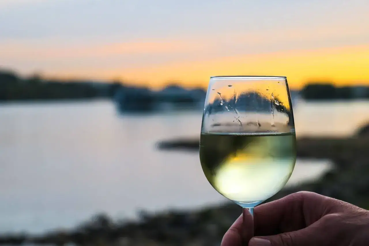 Un verre de vin blanc frais, parfait pour la conservation, tenu à la main au coucher du soleil sur l'eau.