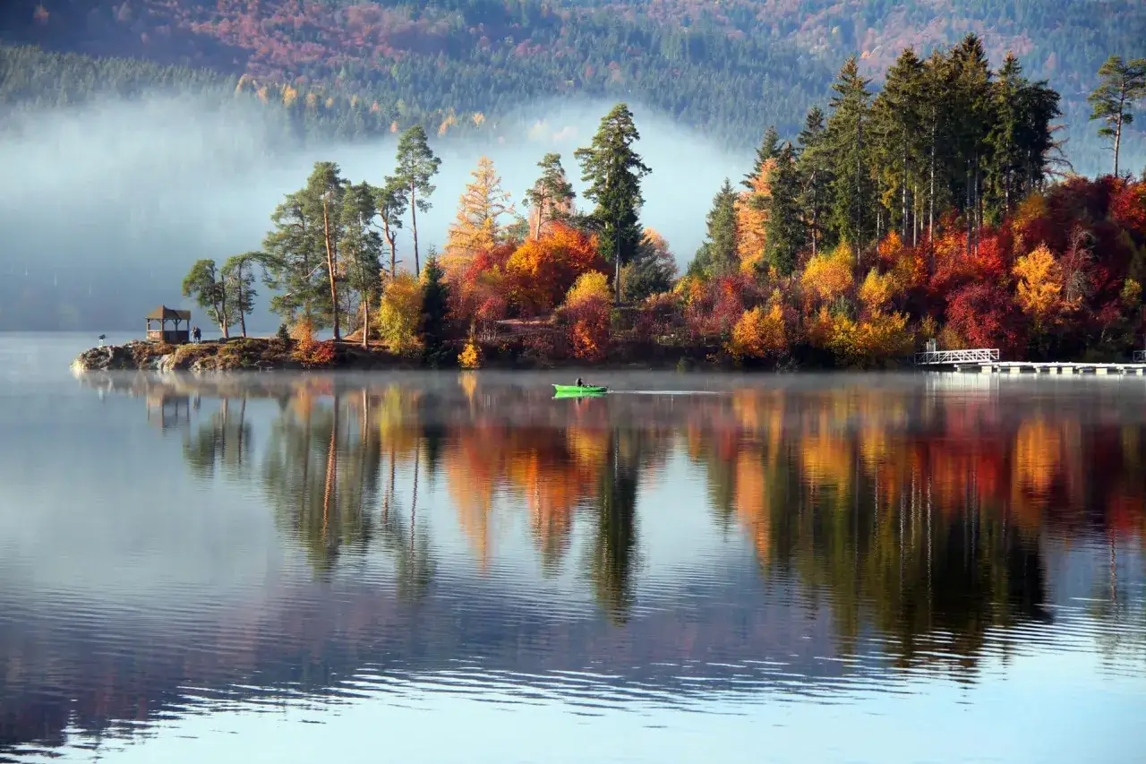 Herbstlicher **Geheimtipp Urlaub November Deutschland**: Nebel &uuml;ber einem See mit bunten B&auml;umen und einem Ruderboot.
