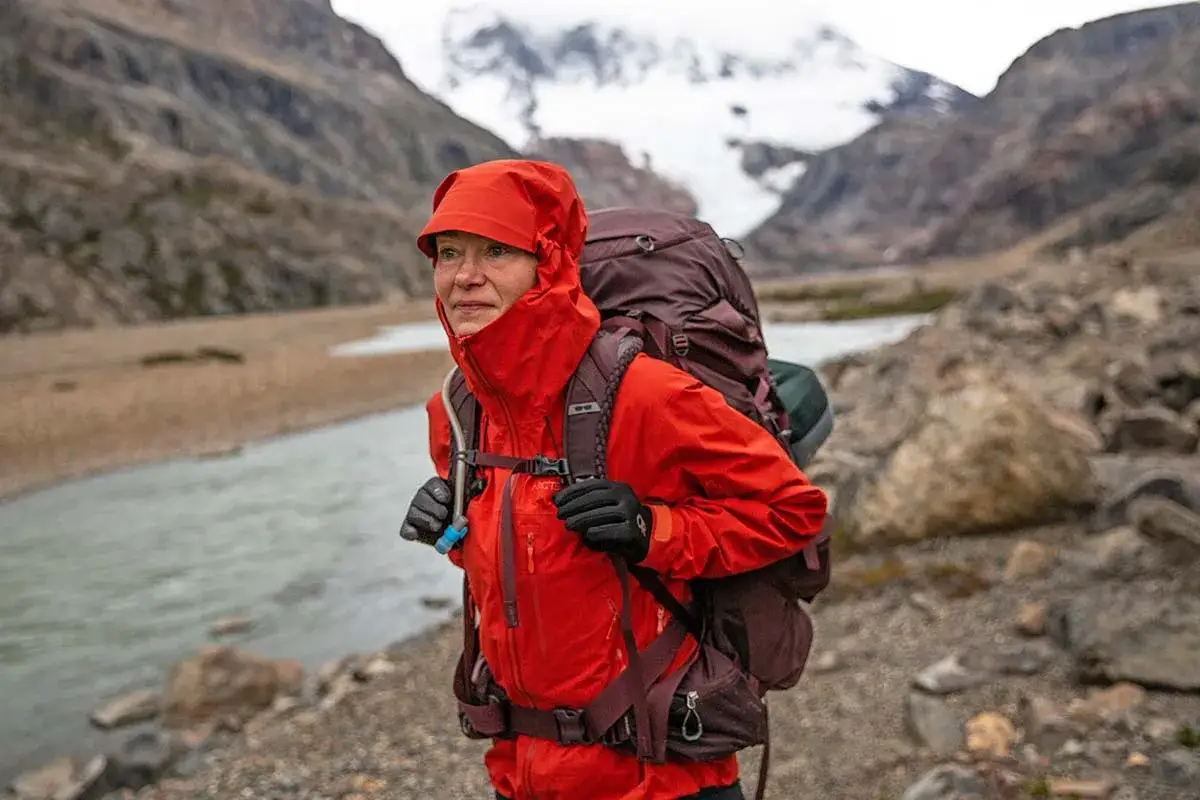 Escursionista con zaino indossa una giacca hardshell rossa, perfetta per proteggersi dagli elementi in montagna.