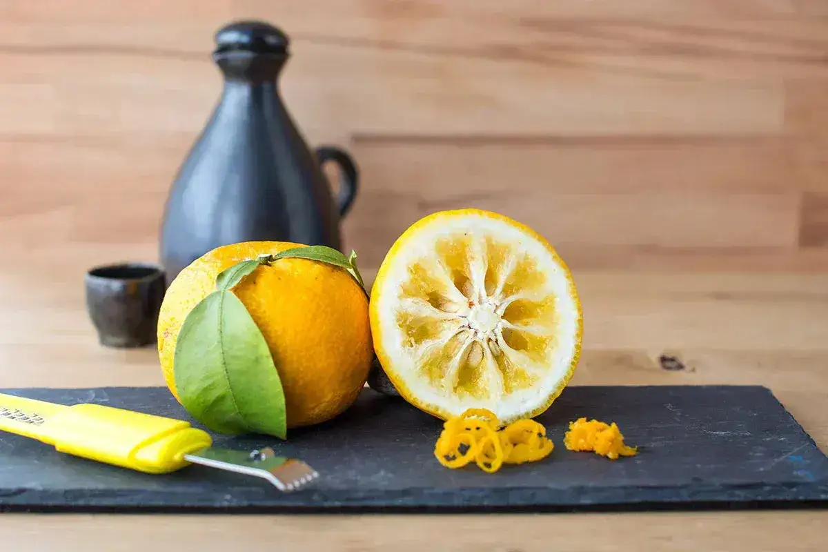 Całe i przekrojone yuzu, obok żółtej obieraczki i skórki. Zastanawiasz się yuzu co to? To cytrus o aromatycznym zapachu.