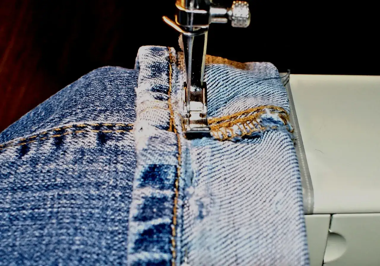 Une machine &agrave; coudre ajuste l'ourlet d'un jean, cr&eacute;ant une nouvelle finition pour un style personnalis&eacute;.