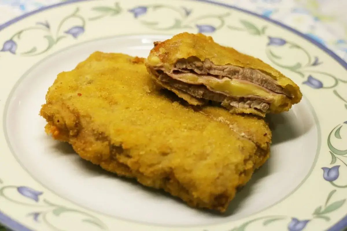 San Jacobo dorado y crujiente, relleno de jam&oacute;n y queso fundido, servido en un plato blanco con decoraciones florales.