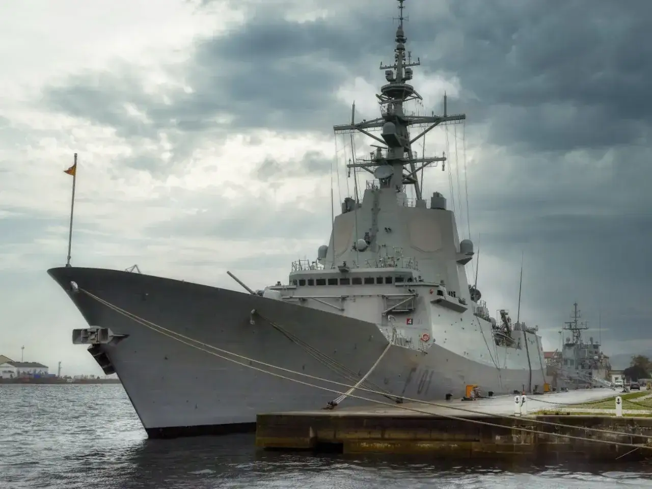 Un imponente buque de guerra gris, quizás donde nació Franco, descansa en el muelle bajo un cielo nublado.
