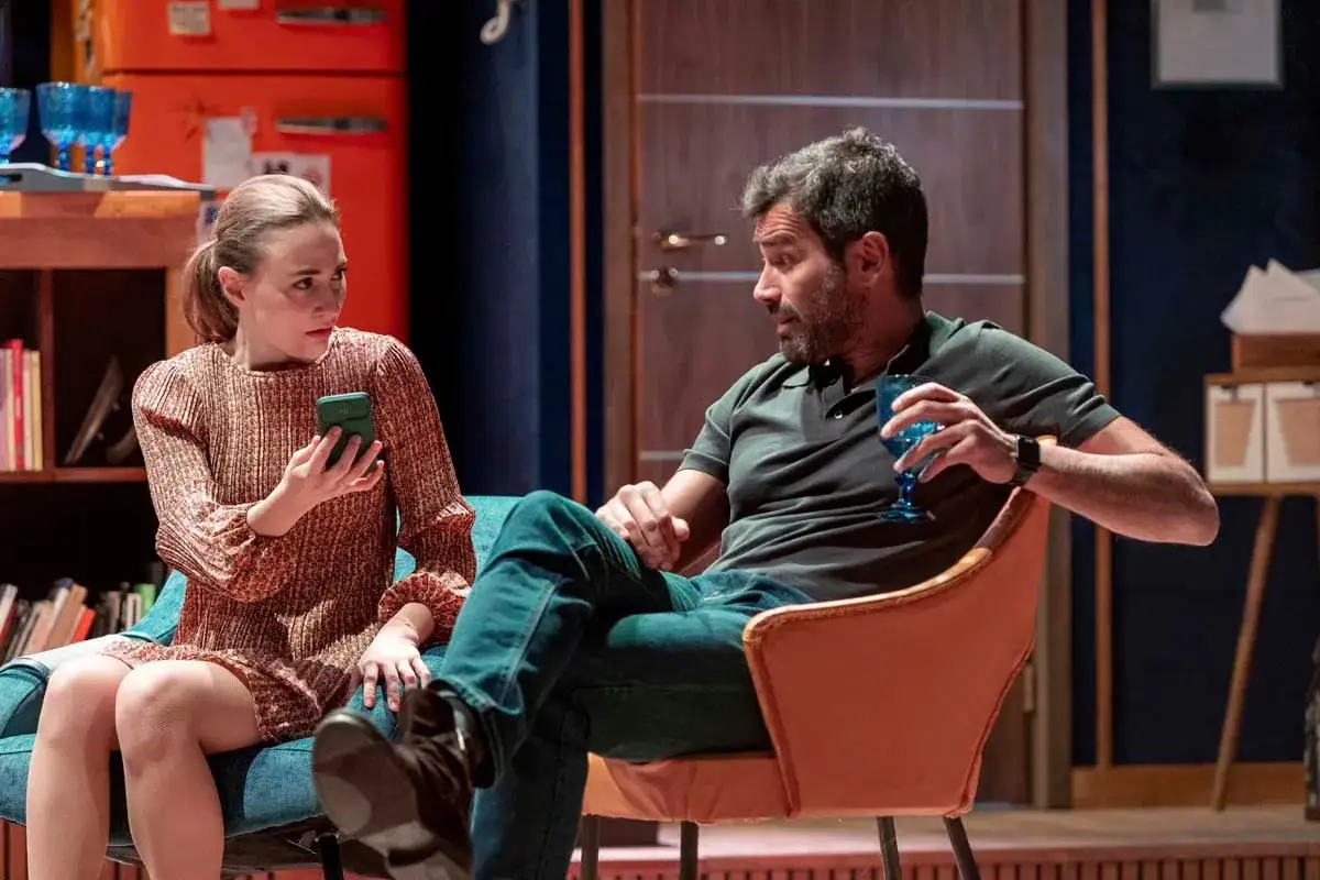 Ambra Jovinelli e un uomo in un dialogo teso, lei guarda il telefono, lui un bicchiere. Perfetti sconosciuti.
