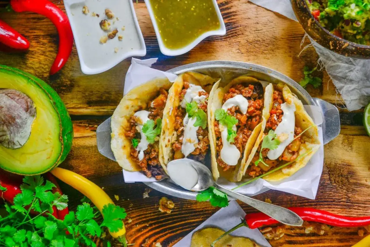 Pyszne tacos z mięsem mielonym, polane kremowym sosem, obok awokado i papryczek chili.