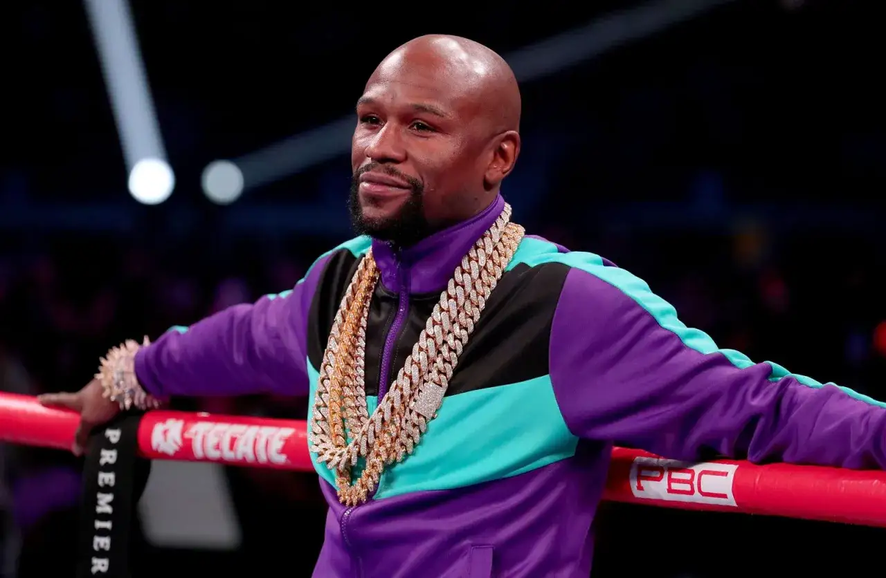 Floyd Mayweather, adorned in diamond chains and a vibrant tracksuit, leans on the ropes. He's been boxing for decades, a true legend.