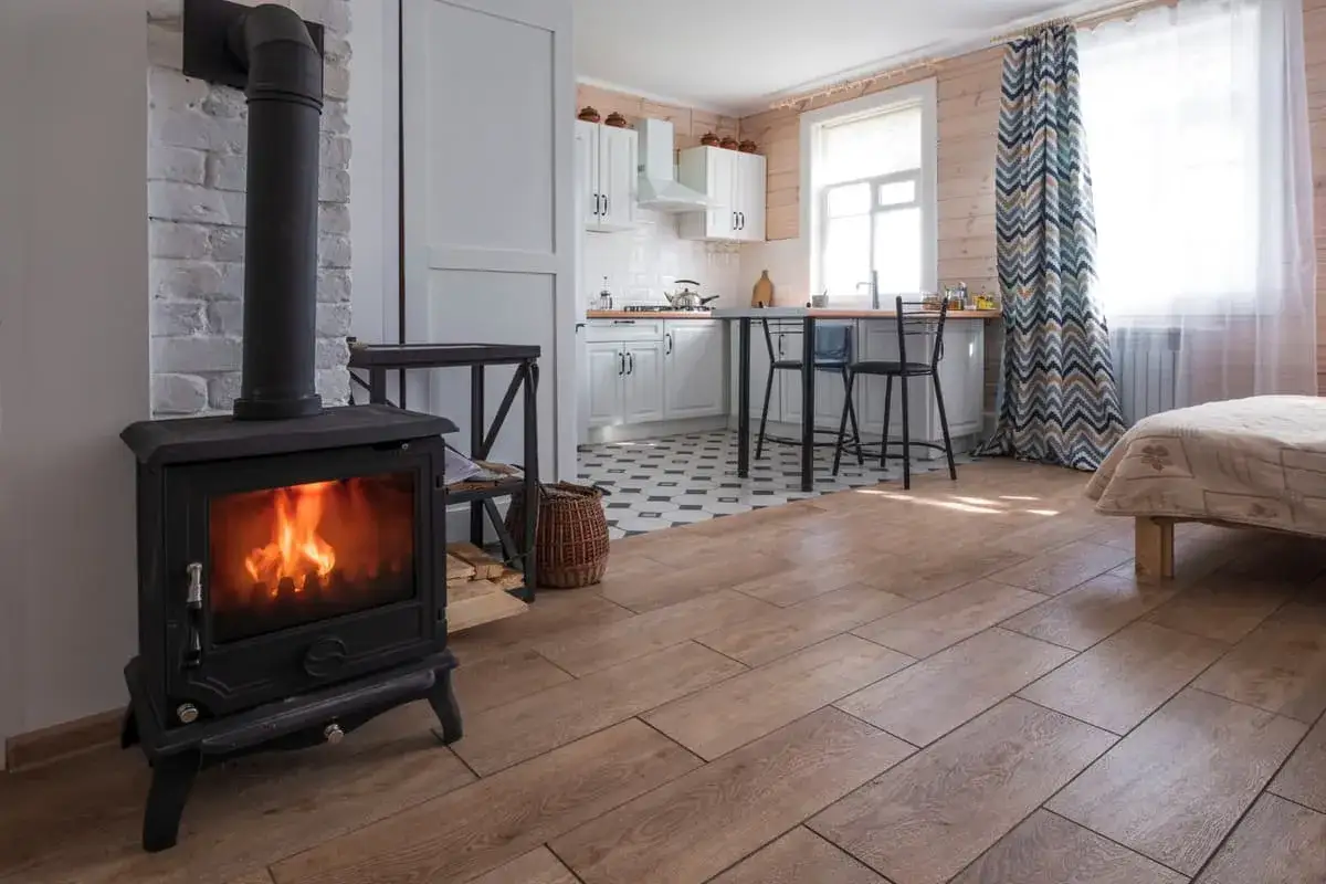 Poêle à bois Prime Renov crépitant dans un salon cosy, avec cuisine ouverte et lit.