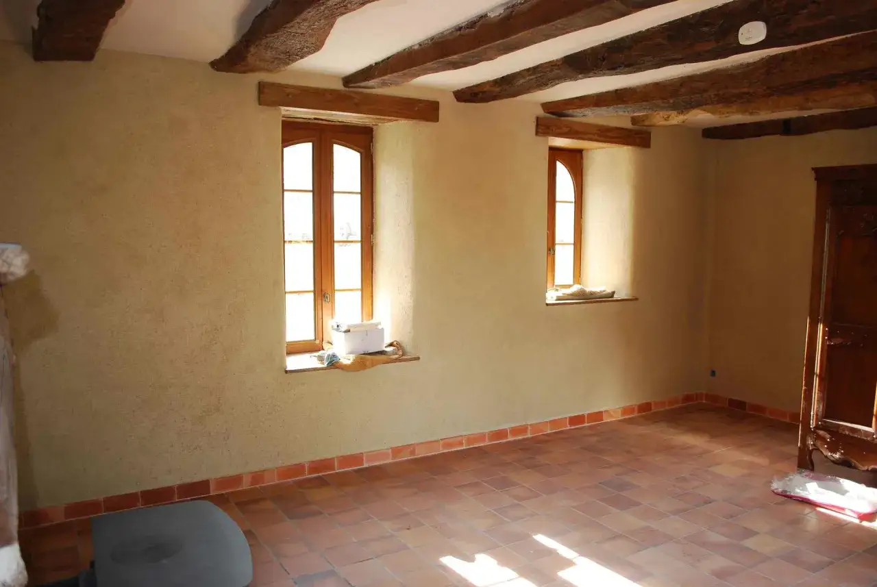 Intérieur d'une maison en pierre en cours de rénovation, avec poutres apparentes, murs texturés et sol en terre cuite.