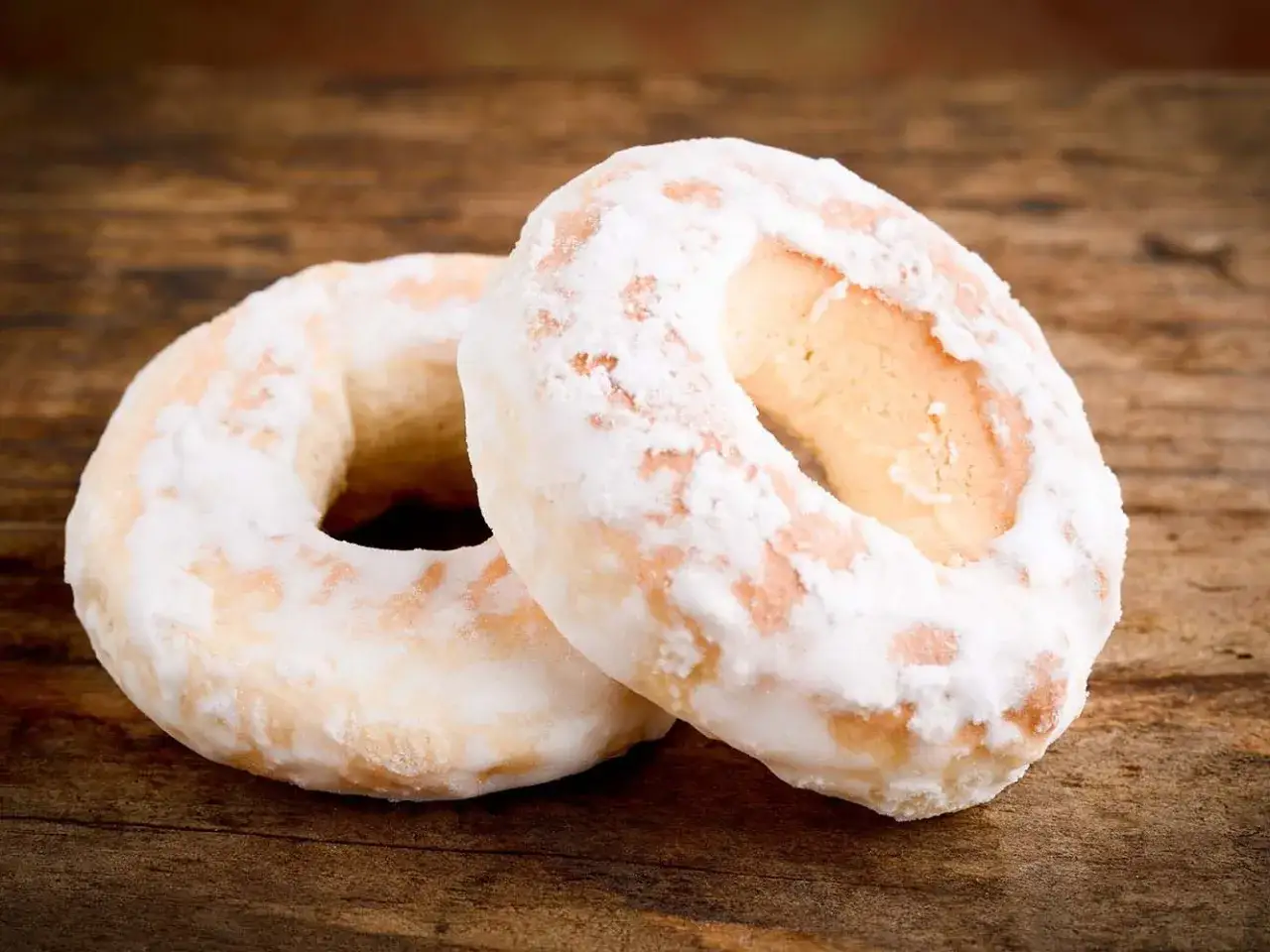 Due taralli dolci, cosparsi di zucchero a velo, riposano su un tavolo di legno rustico.