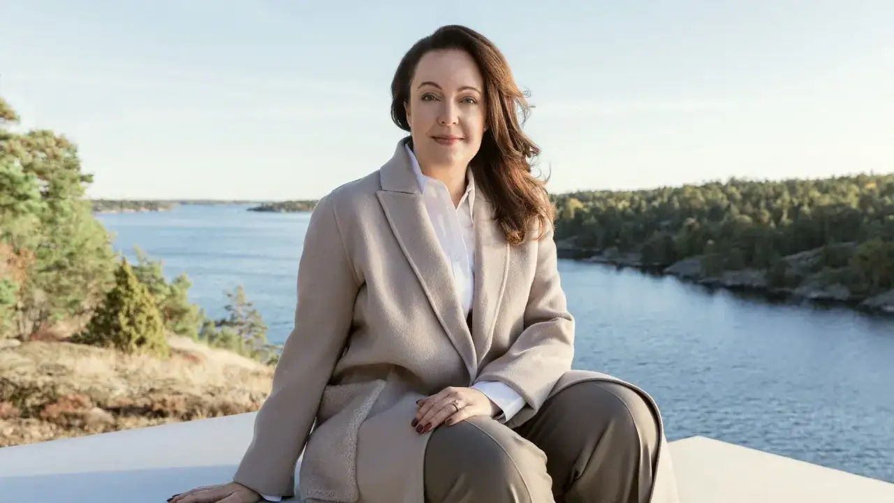 Anna Borg sitter p&aring; en mur med en vacker sk&auml;rg&aring;rdsmilj&ouml; bakom sig.