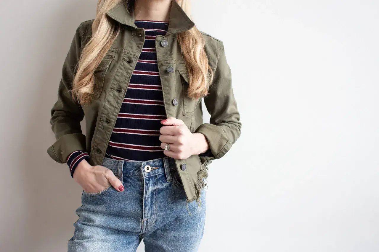 En kvinna i en grön jacka och randig topp, redo för vårmode 2026 dam. Jeans och en avslappnad stil.