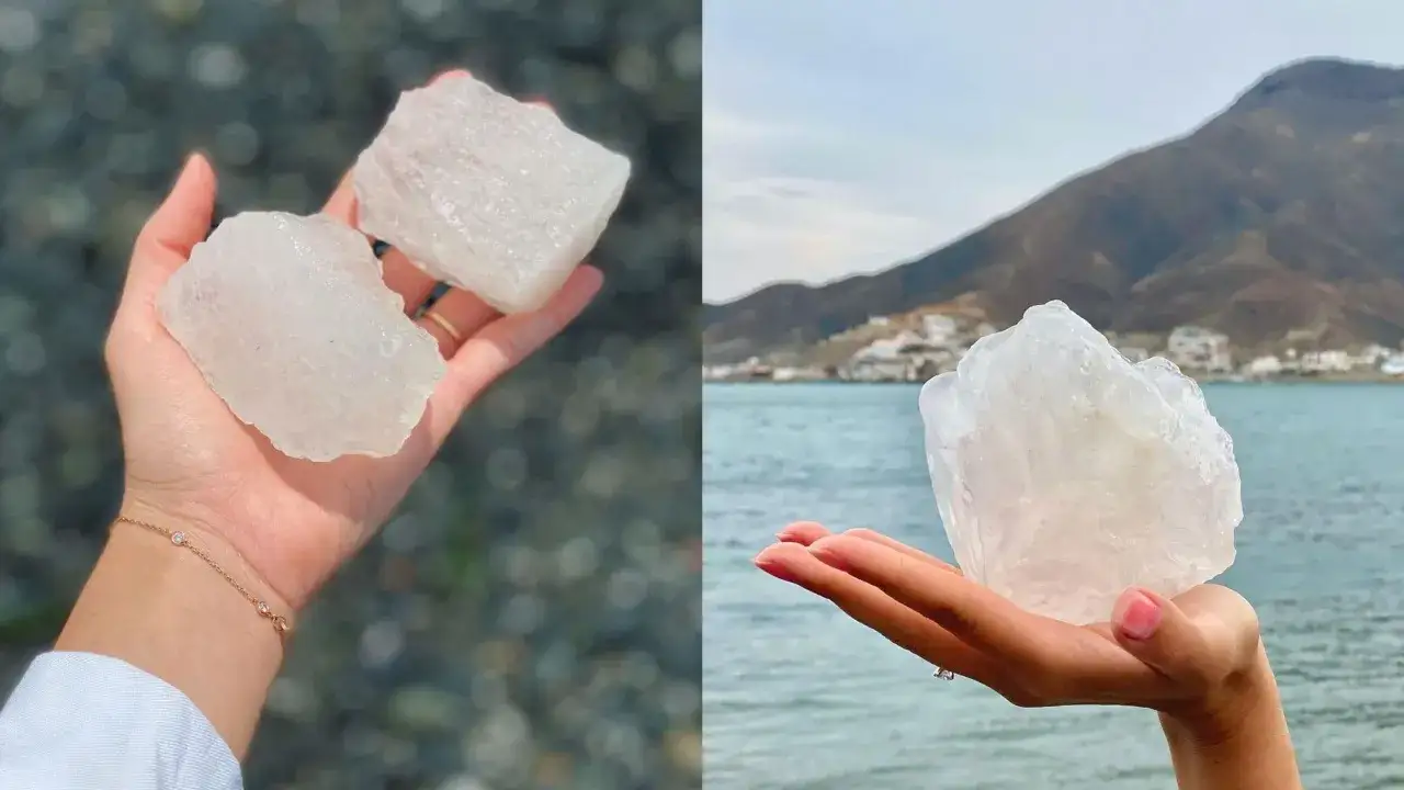 Manos sostienen trozos de piedra alumbre transl&uacute;cida, uno con dos piedras sobre fondo de guijarros, otro con una piedra frente al mar y monta&ntilde;as.