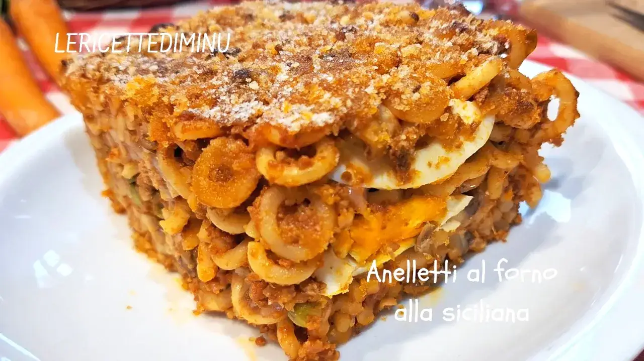 Porzione di anelletti al forno alla siciliana, con strati di pasta, rag&ugrave; e uova sode, dorata in superficie.