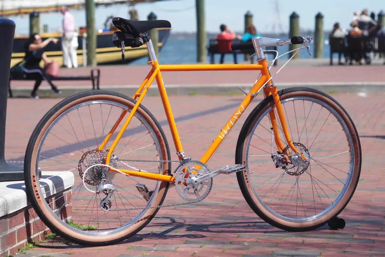 An orange Velo Orange city bike with tan tires and disc brakes, ready for urban adventures.