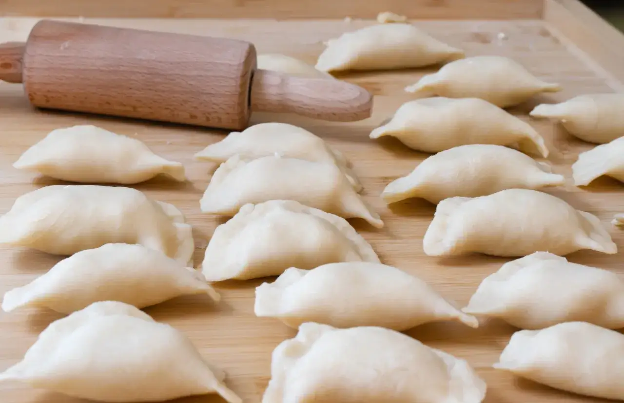 Gotowe do lepienia pierogi, ułożone na desce obok drewnianego wałka. Ciasto na pierogi czeka na nadzienie.