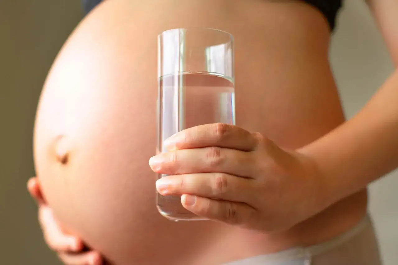 Schwanger, mit einem Glas Wasser in der Hand. Bei Durchfall in der Schwangerschaft ist Flüssigkeitszufuhr wichtig.