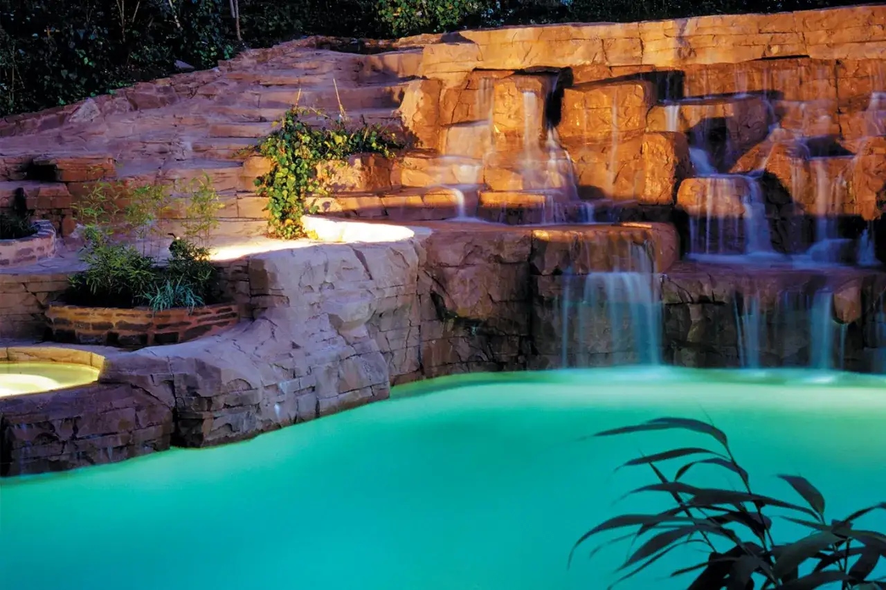 Un magnifique exemple de cascade pour bassin, avec des rochers sculptés et une eau turquoise invitante.