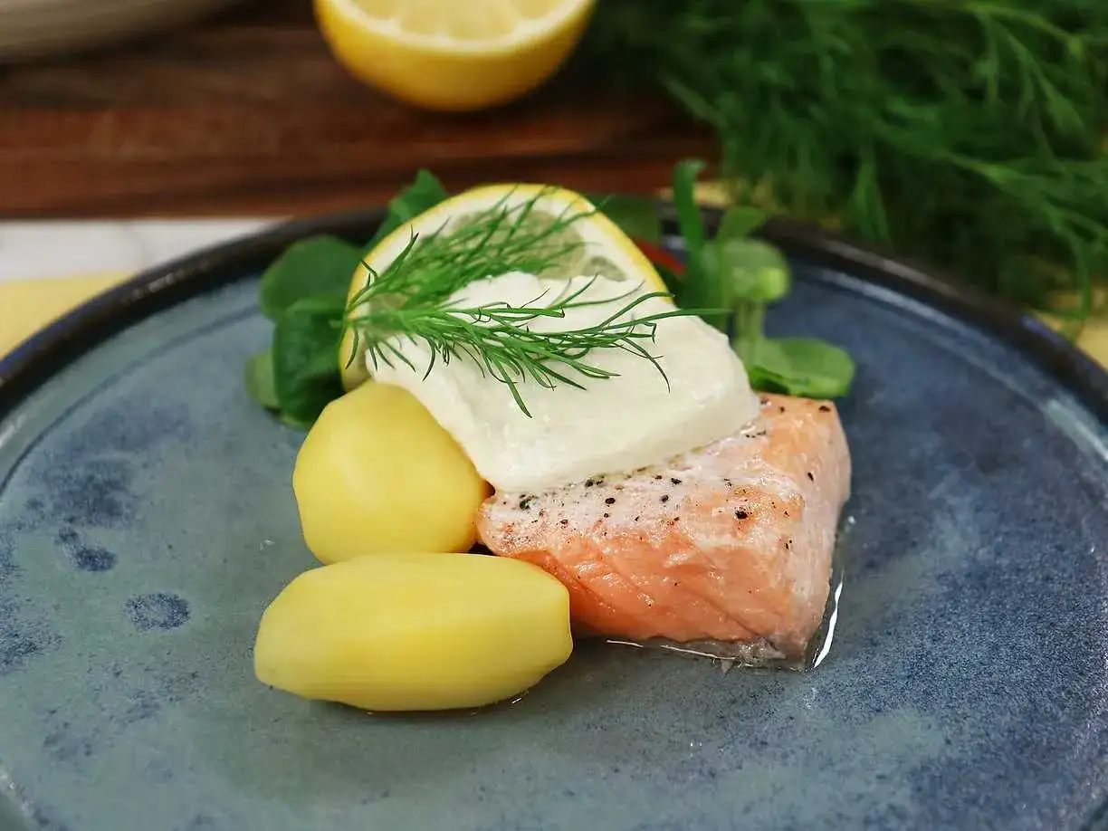 En bit lax med romsås, dill och kokt potatis på en blå tallrik. En klassisk svensk rätt.