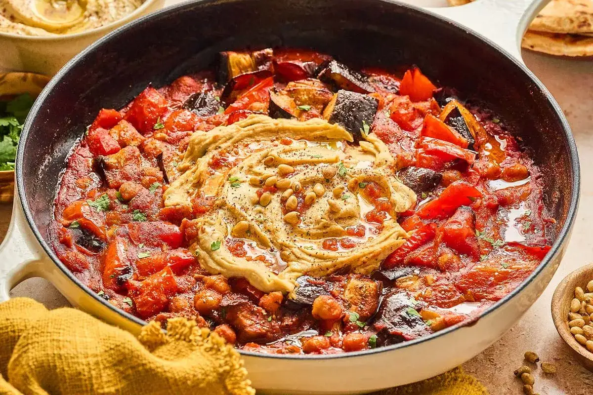 Plat mijoté de légumes et pois chiches, garni de houmous crémeux et de pignons de pin. Une délicieuse recette pois chiche à partager.