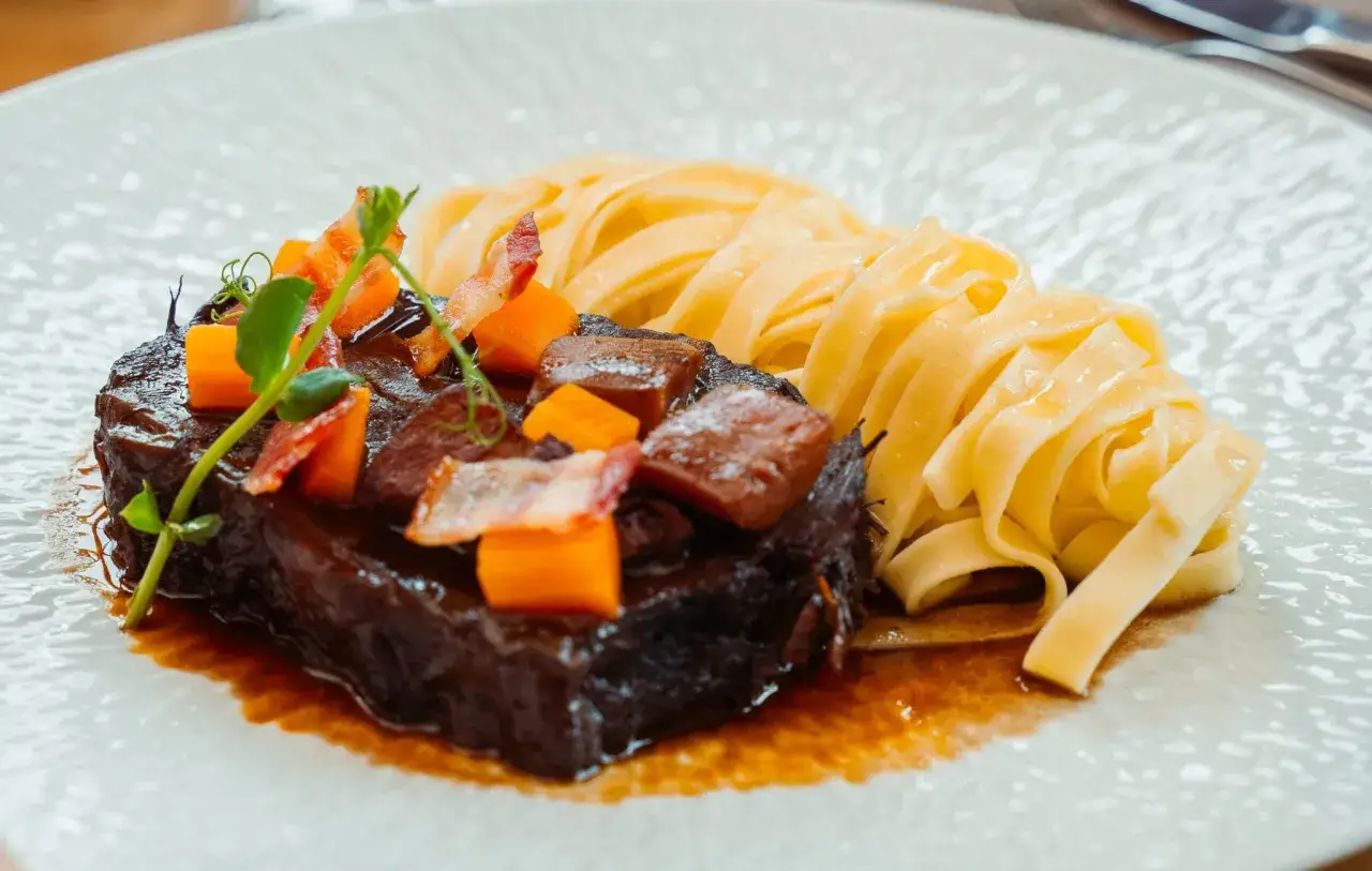 Un généreux paleron de boeuf braisé, garni de dés de carottes et de lardons, servi avec des tagliatelles fraîches.