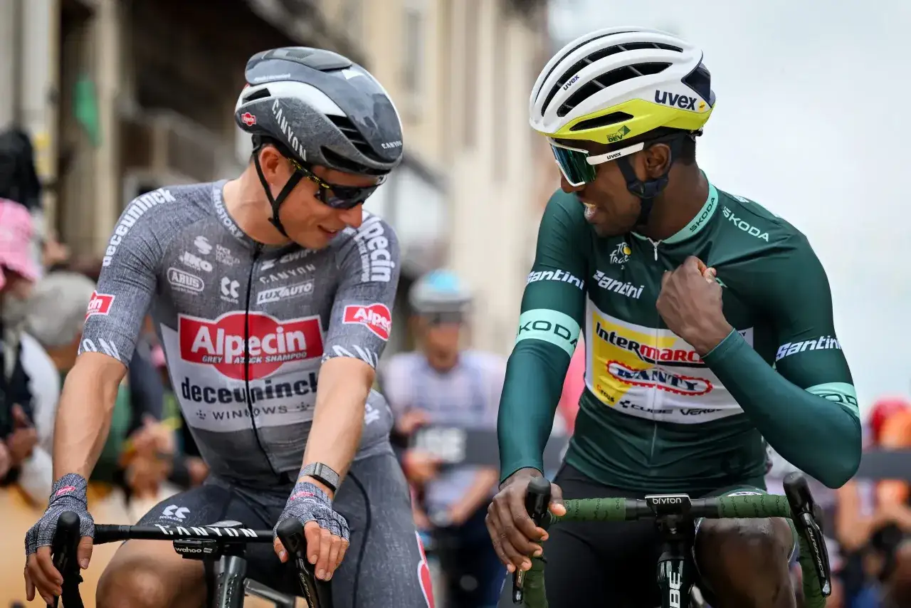Two cyclists in racing gear, one in a grey jersey and the other in a green jersey, chat during the Tour de France.