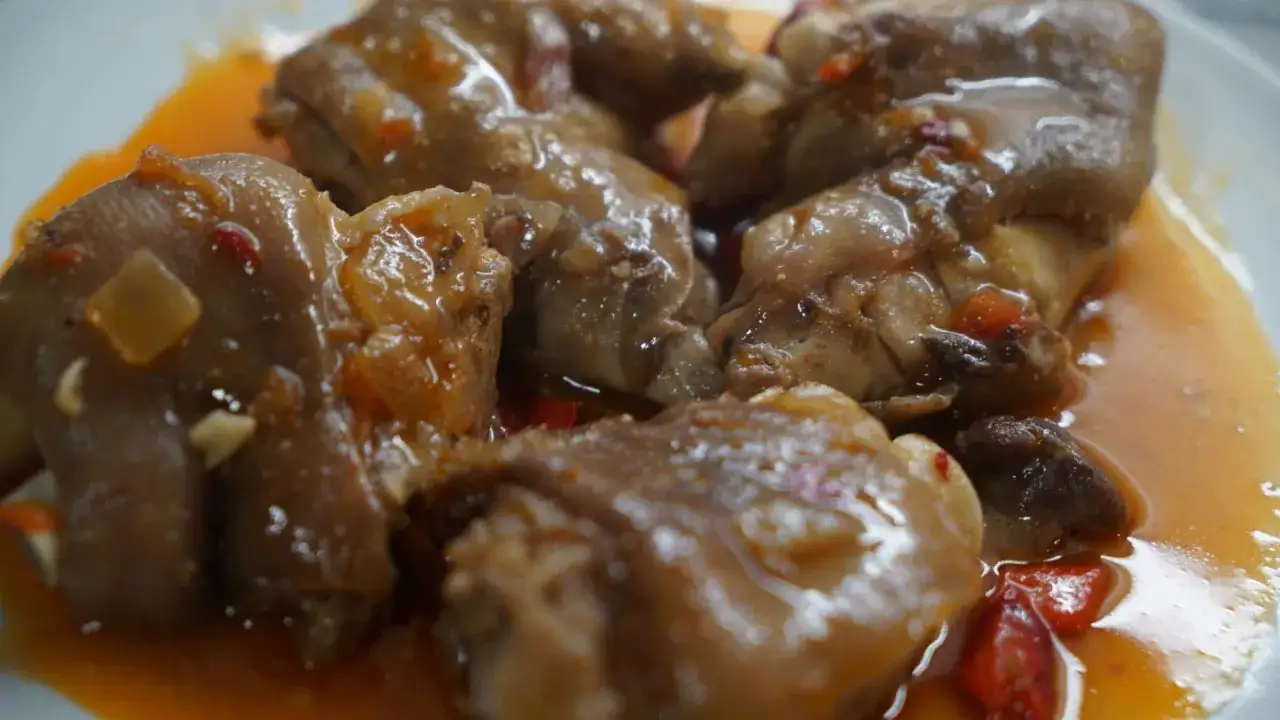 Manitas de cerdo en salsa, un plato tradicional de comida t&iacute;pica de Valladolid, con trozos de pimiento y cebolla.