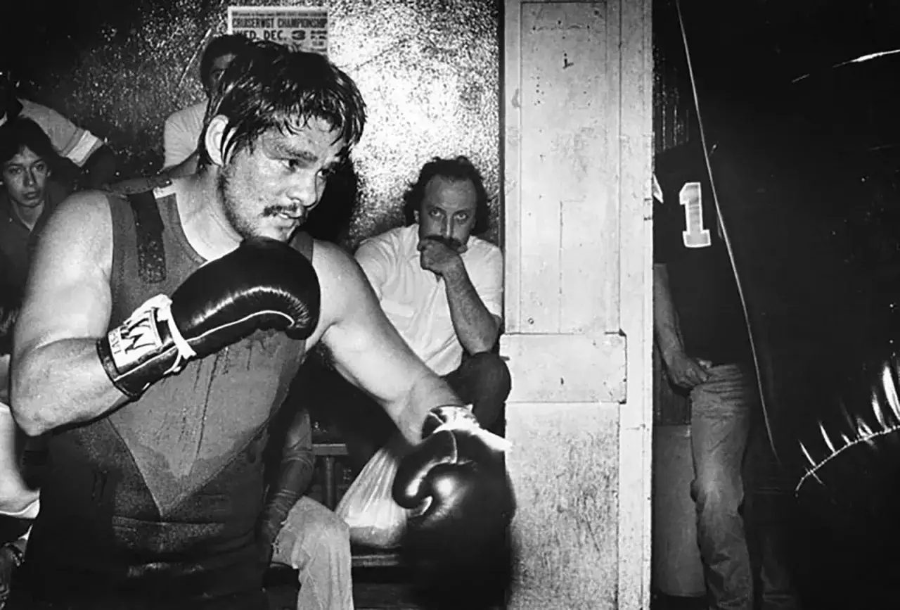Young Roberto Duran trains intensely, sweat dripping as he throws a punch. A poster for a championship fight hangs in the background.