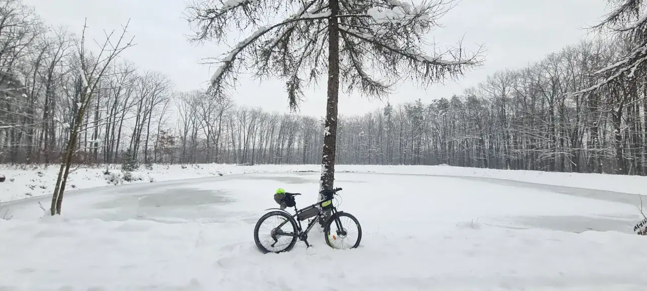 Rower czeka na wiosnę nad zamarzniętym jeziorem. Zimowe trasy rowerowe Tarnów kuszą pięknem przyrody.
