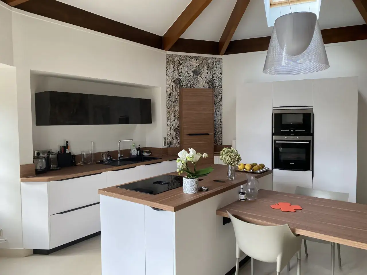 Cuisine moderne avec des meubles blancs et un **cr&eacute;dence et plan de travail assortis** en bois. Une table en bois avec des chaises claires est install&eacute;e.