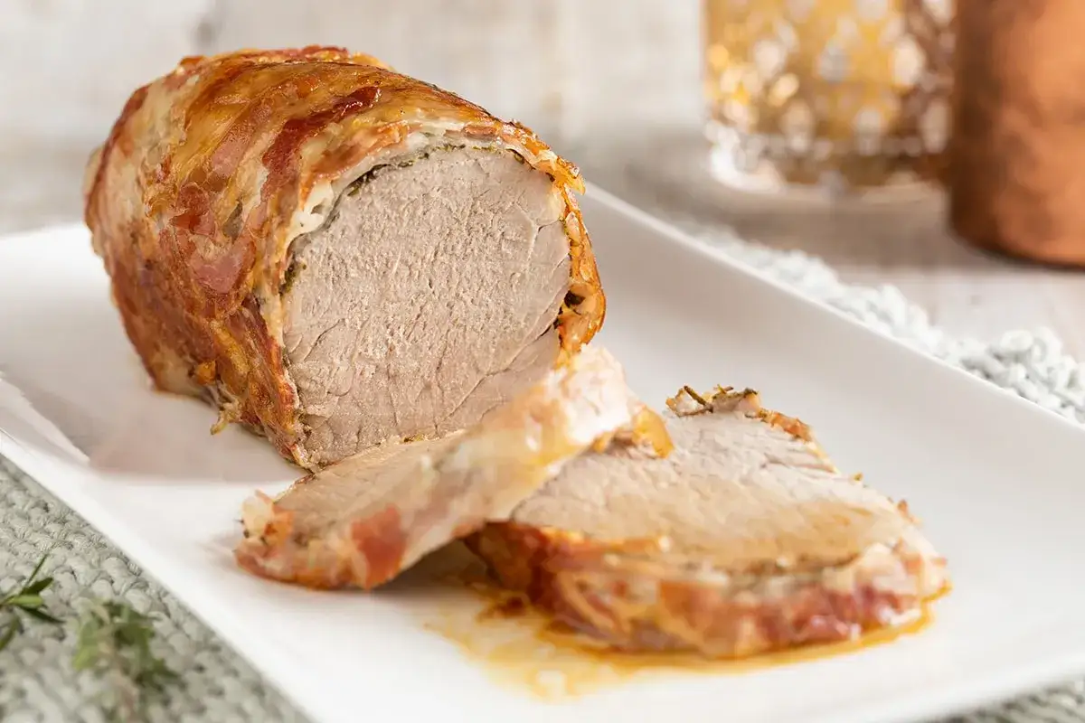 Succulento filetto al forno, avvolto in pancetta croccante, servito su un piatto bianco con fette tagliate.
