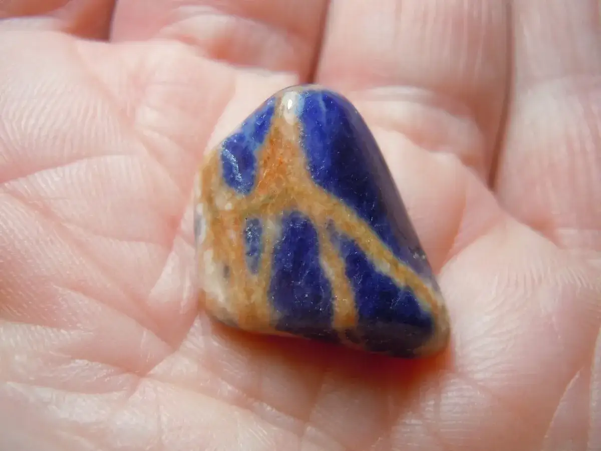 Una pietra di sodalite blu e arancione, con venature che ricordano un fulmine, tenuta in mano. Le sue propriet&agrave; sono note per la calma.