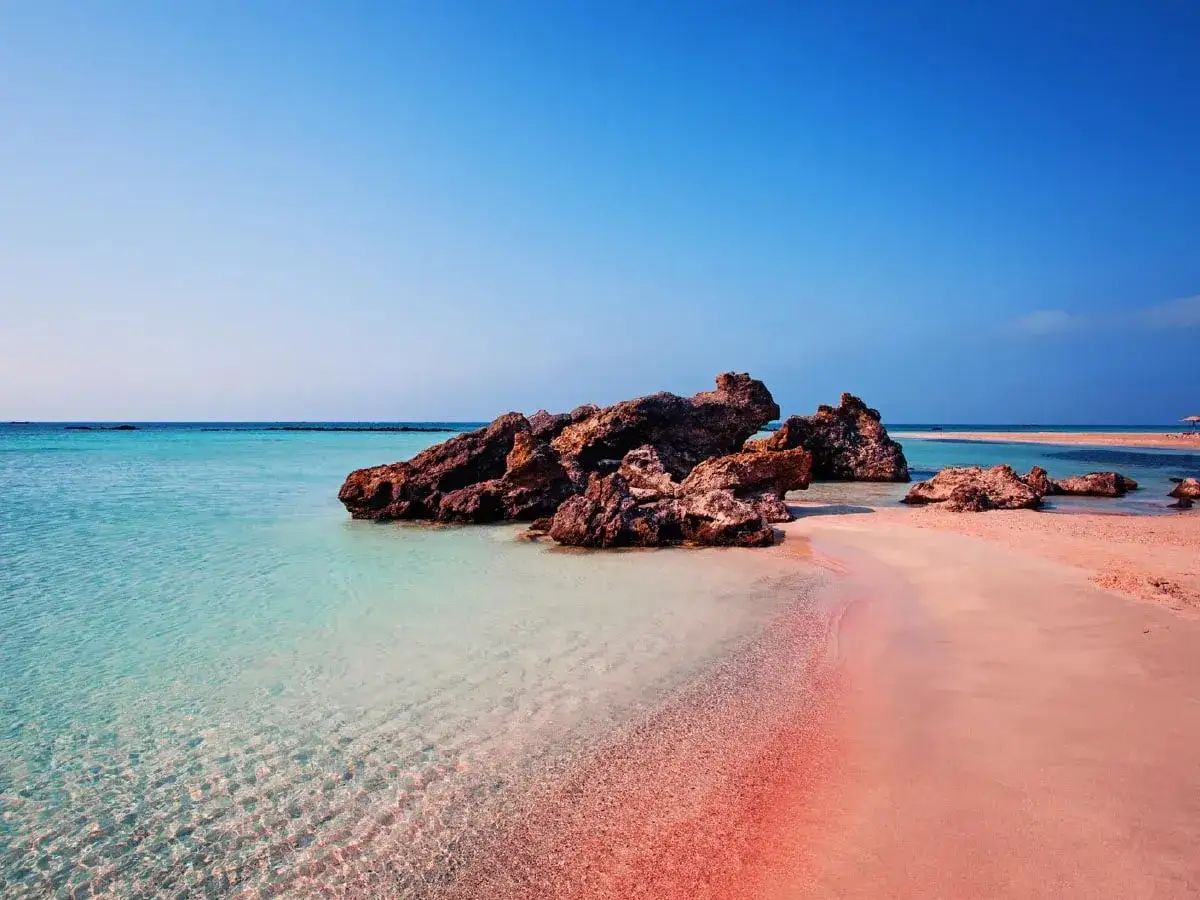 Traumhafter Strand auf Kreta mit rosa Sand, t&uuml;rkisfarbenem Wasser und Felsen. Ein idyllischer Ort zum Entspannen.