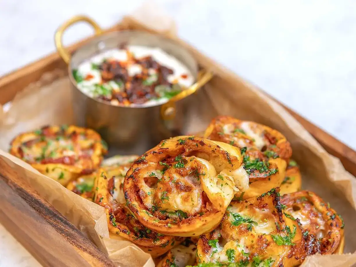 Pizzabullar recept: Gyllene, ostiga pizzabullar med f&auml;rsk persilja, serverade med en kr&auml;mig dipp i en tr&auml;l&aring;da.