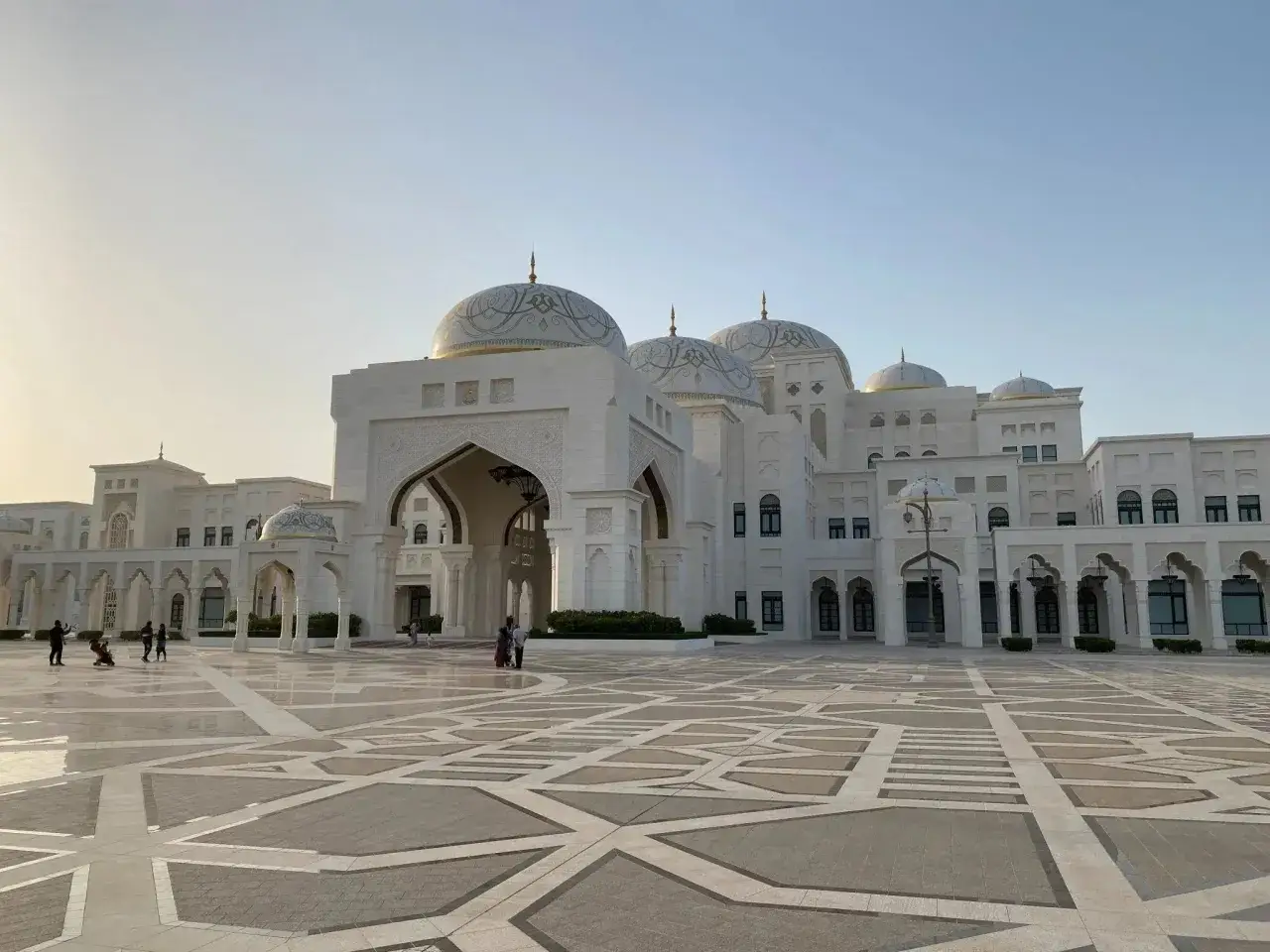 Majestatyczny Qasr Al Watan z białego kamienia, z kopułami i łukami, na tle błękitnego nieba.