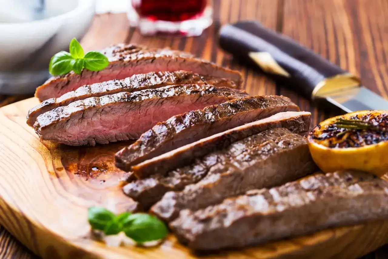Skivad flapsteak med perfekt medium-rare temp, garnerad med basilika och serverad med grillad citron.