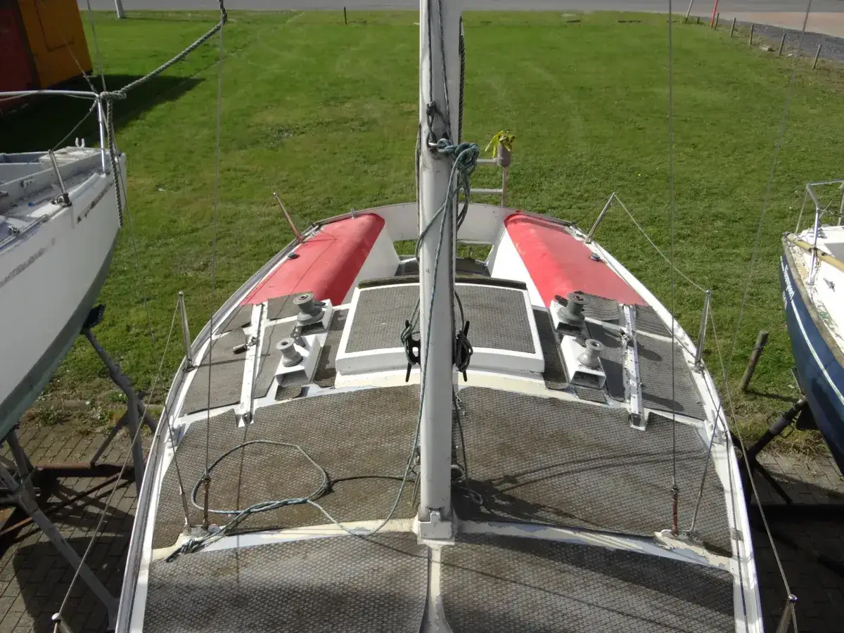 Vue aérienne du pont d'un voilier, peut-être un Pen Duick 600, avec ses winchs et sa grand-voile enroulée.