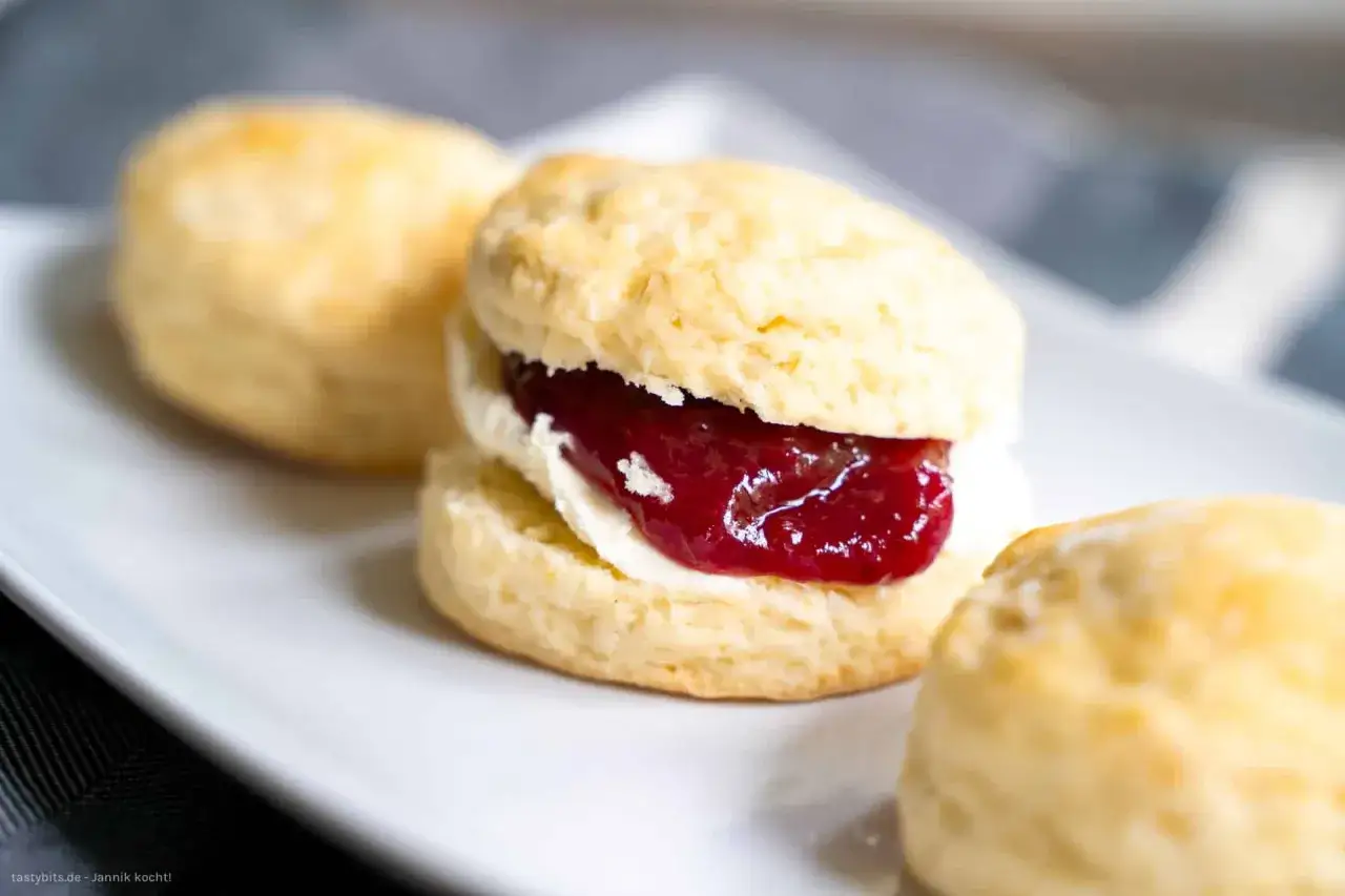 Frisch gebackene Scones, der Teig perfekt aufgegangen, gefüllt mit Clotted Cream und roter Marmelade. Ein Genuss!