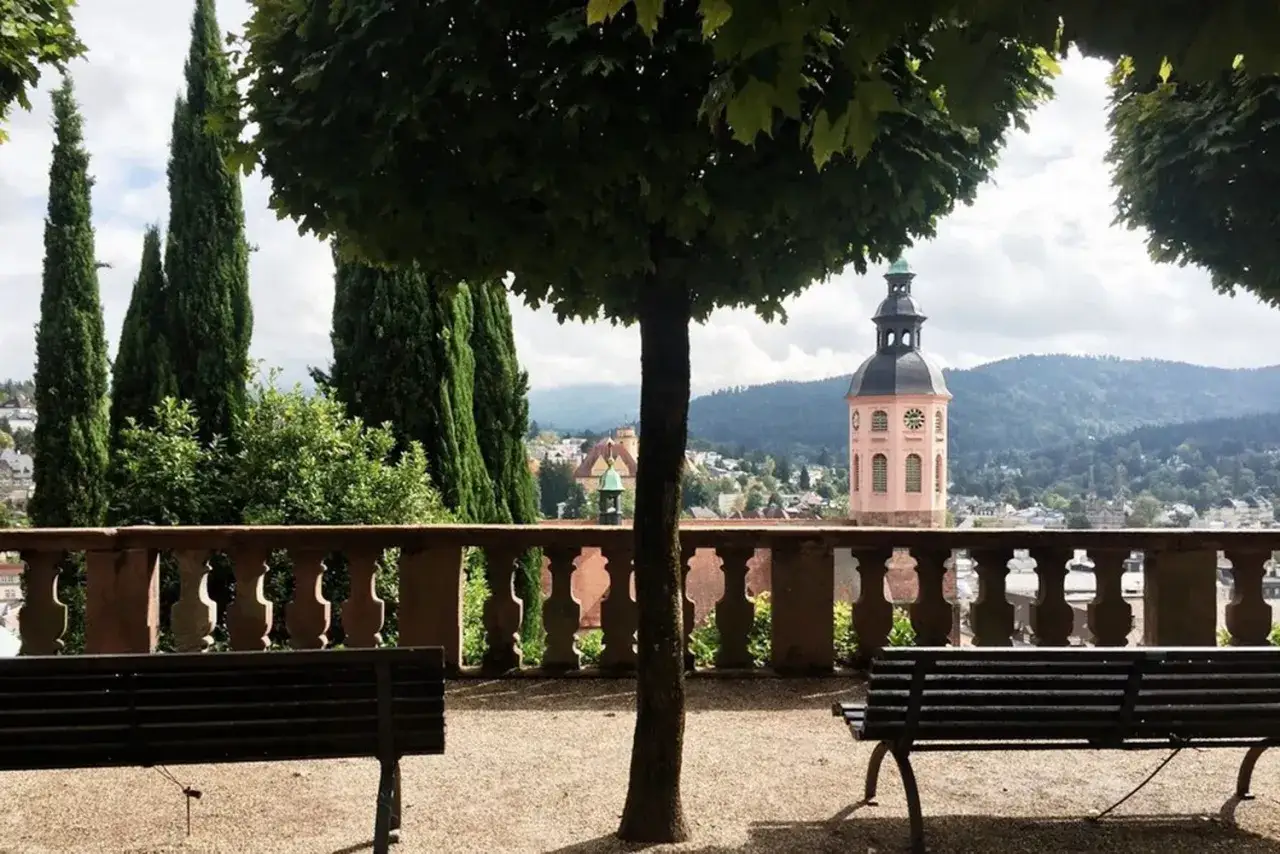 Ein friedlicher Tag in Baden-Baden. Zwei B&auml;nke laden zum Verweilen ein, w&auml;hrend im Hintergrund ein Kirchturm und gr&uuml;ne H&uuml;gel die Aussicht zieren.
