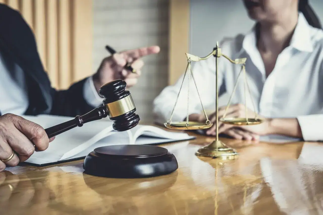 Prawnik wyjaśnia klientce kwestie rozdzielności majątkowej a śmierci małżonka. Na stole młotek sędziowski i waga sprawiedliwości.