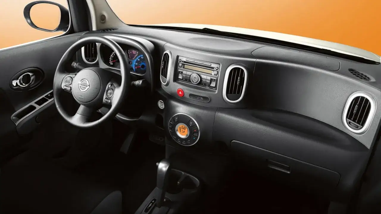 Wnętrze Nissan Cube: kierownica, radio, klimatyzacja i dźwignia zmiany biegów.