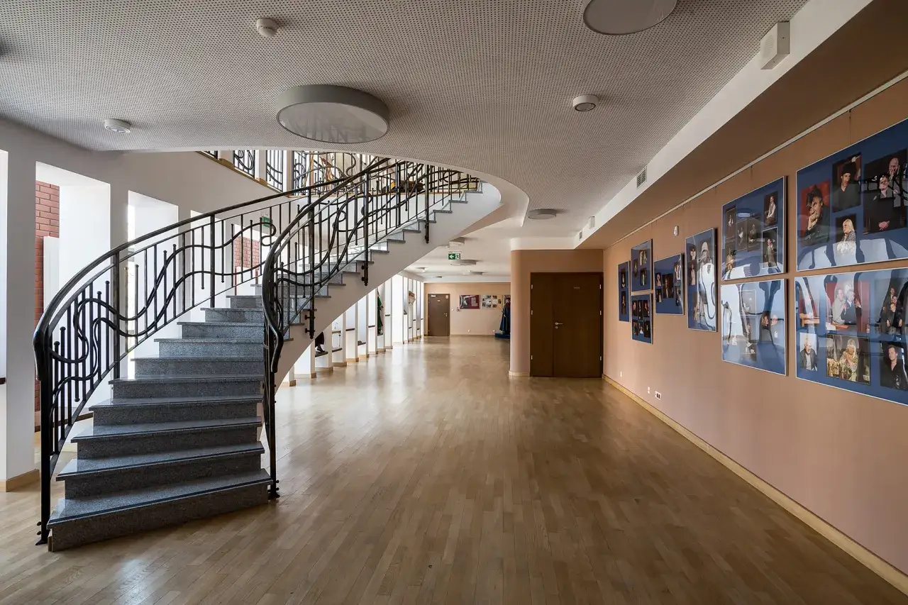 Eleganckie foyer teatru ze schodami i galerią zdjęć. Czasem zastanawiamy się, ile trwa spektakl w teatrze, ale to foyer też ma swój urok.
