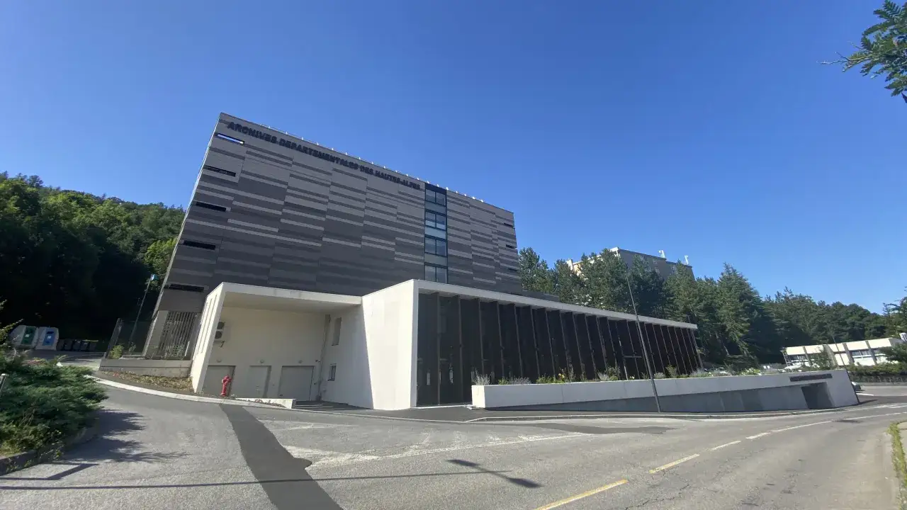 B&acirc;timent moderne des Archives d&eacute;partementales des Hautes-Alpes, avec une fa&ccedil;ade grise &agrave; rayures et une partie blanche en b&eacute;ton.