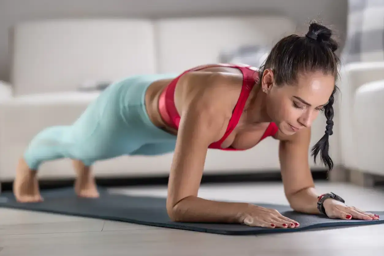 Mujer en posici&oacute;n de plancha, ejercit&aacute;ndose para quitar barriga menopausia.